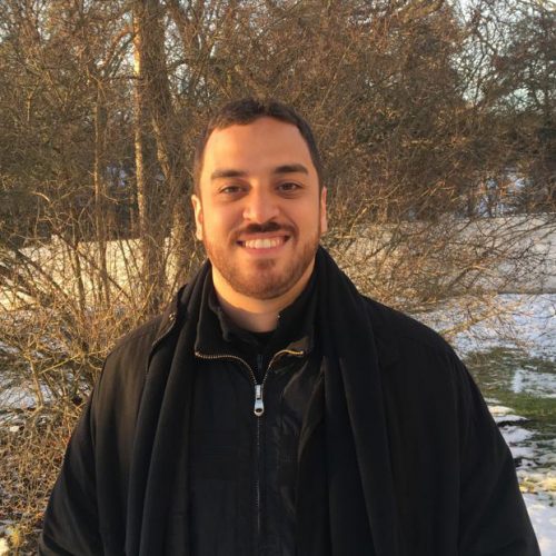 Luigi Parrini em pé, sorrindo e com roupas de inverno, na frente de árvores sem folhas e chão coberto de neve